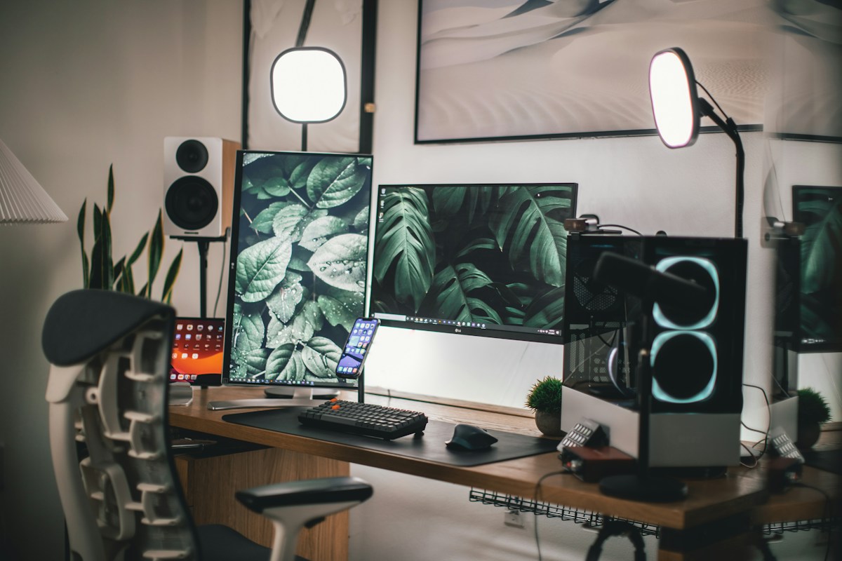 A home desk with dual screens, speakers, and a lamp